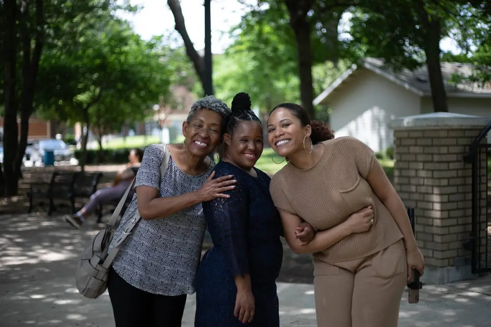 Three women of different ages laugh together outdoors.