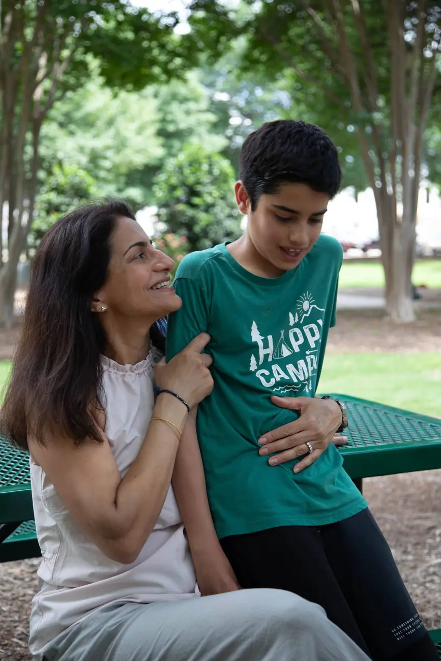 A mother and her teenage son laugh together on a park bench.
